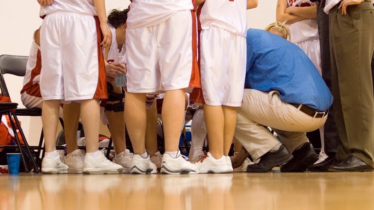 Girl basketball players huddle around coach squatting down instructing team