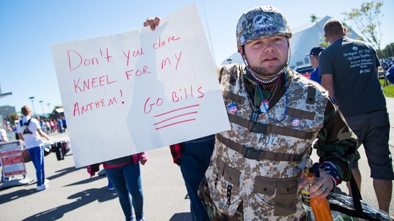 Fan dressed in camouflage holds sign protesting players kneeling for the national anthem