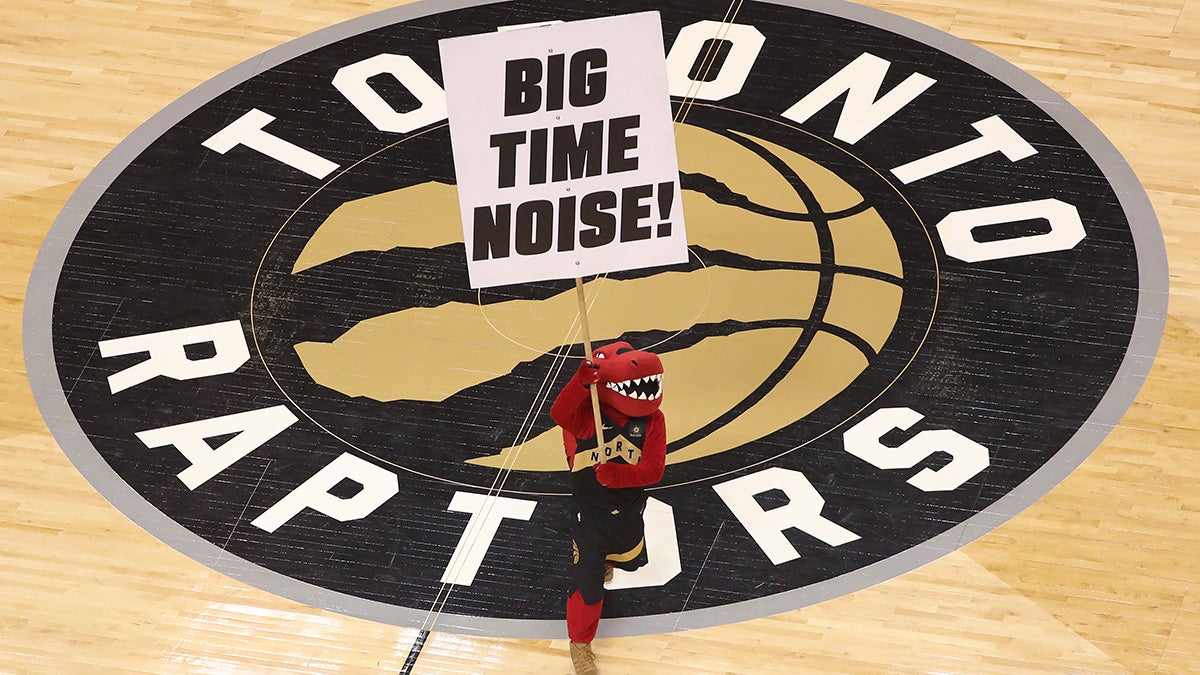 Raptor the mascot of the Toronto Raptors holds a sign at center court imploring fans to make noise over the team logo.