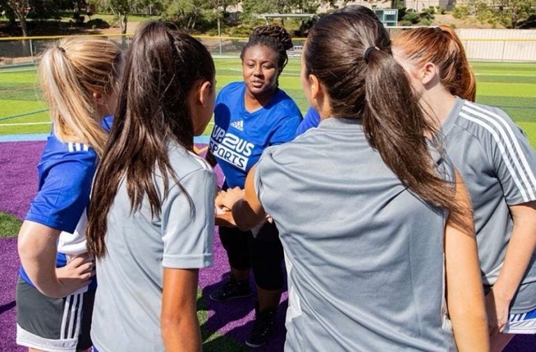 A group of female athletes on a field, with their hands in a huddle. (Photo courtesy of Up2Us Sports)